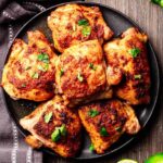 Perfectly baked Mexican chicken thighs with crispy, golden skin, garnished with fresh cilantro and served on a black plate, placed on a rustic wooden surface.