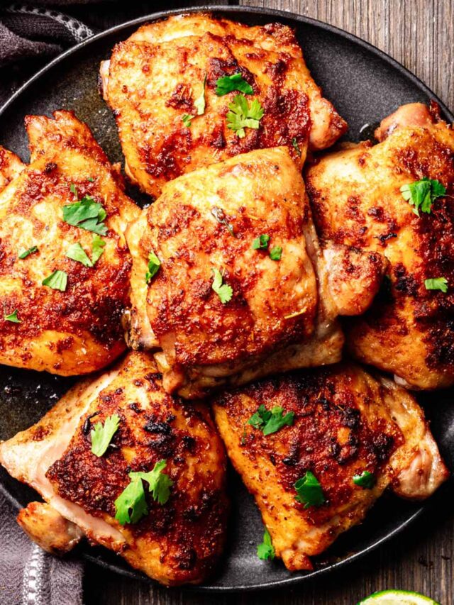 Perfectly baked Mexican chicken thighs with crispy, golden skin, garnished with fresh cilantro and served on a black plate, placed on a rustic wooden surface.