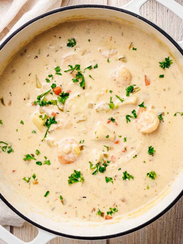 Overhead view of a creamy seafood chowder in a white Dutch oven, featuring shrimp, diced potatoes, and fresh parsley garnish.