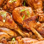 Close-up view of juicy chicken adobo drumsticks glistening in a savory sauce, garnished with fresh green onion slices for a burst of color.