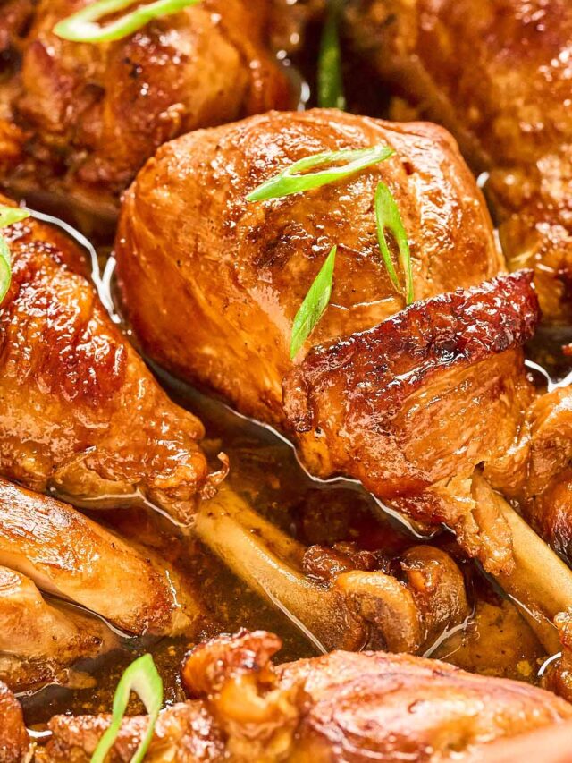 Close-up view of juicy chicken adobo drumsticks glistening in a savory sauce, garnished with fresh green onion slices for a burst of color.