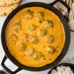 A black skillet filled with Chicken Curry Meatballs simmering in a creamy red curry sauce, garnished with fresh cilantro, served alongside naan bread and a bowl of white rice.