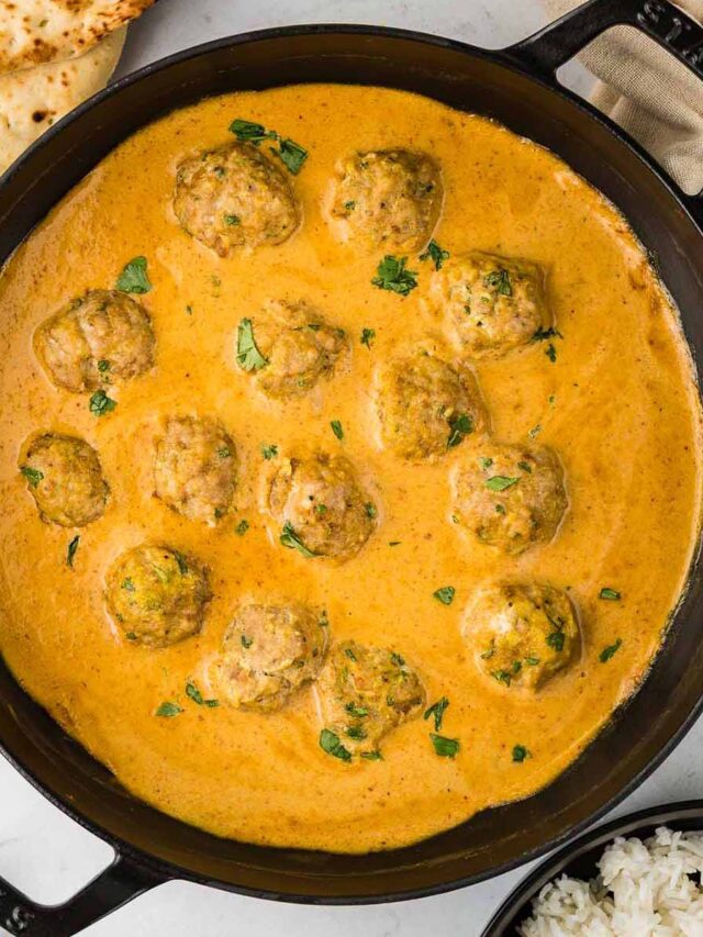 A black skillet filled with Chicken Curry Meatballs simmering in a creamy red curry sauce, garnished with fresh cilantro, served alongside naan bread and a bowl of white rice.