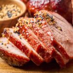Close-up of five-spice pork slices, garnished with sesame seeds and served on a wooden board, with a small bowl of sesame seeds in the background.