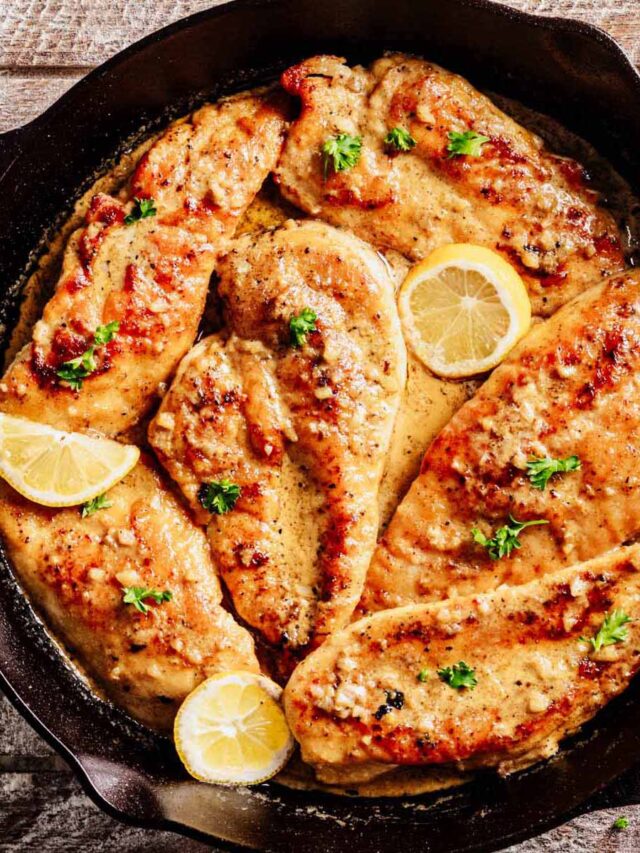 Overhead view of Limoncello Chicken in a cast iron skillet, featuring golden seared chicken breasts coated in a creamy citrus sauce, garnished with fresh parsley and lemon slices.
