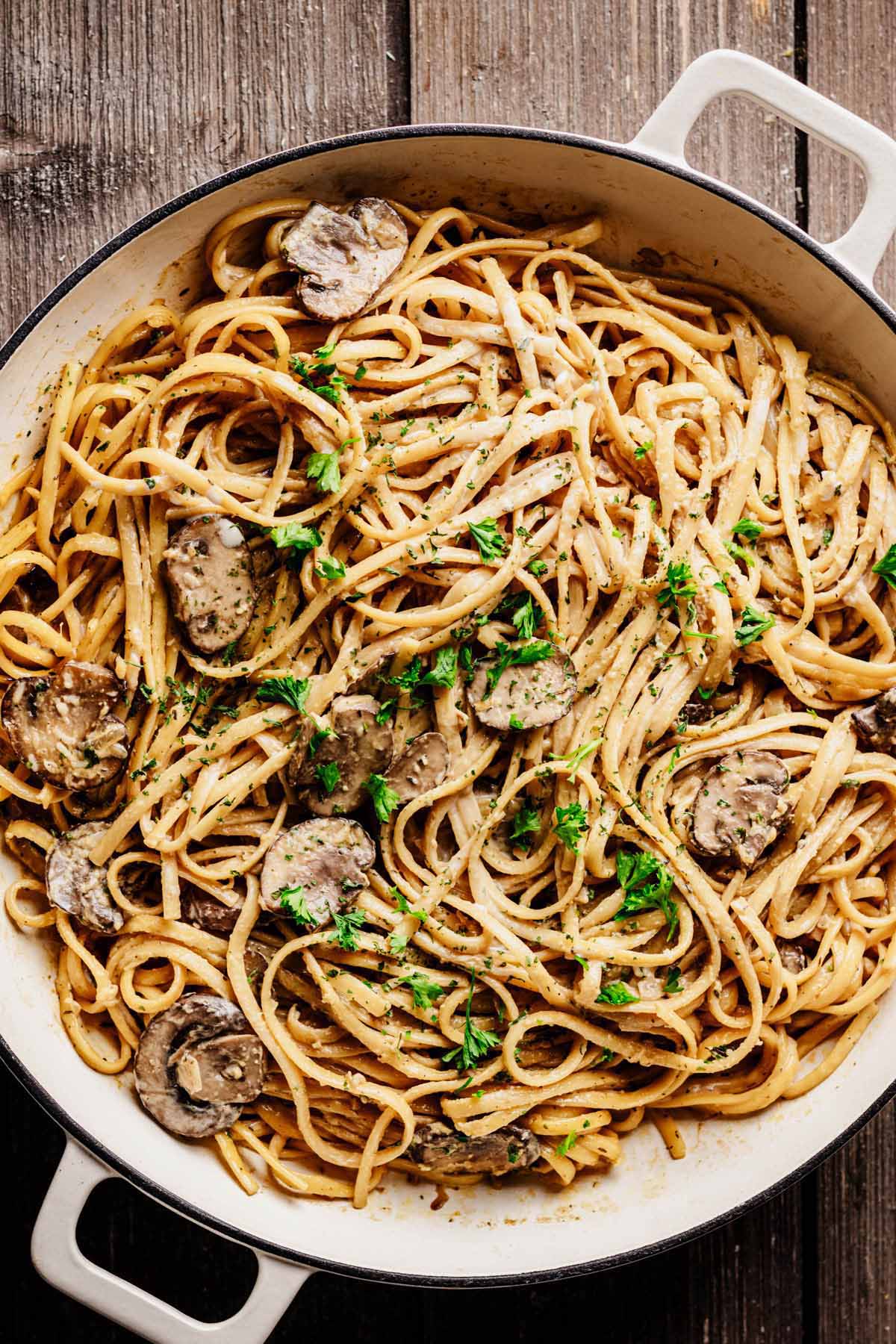 Large white skillet filled with creamy one-pot mushroom pasta, garnished with fresh parsley and sliced mushrooms.