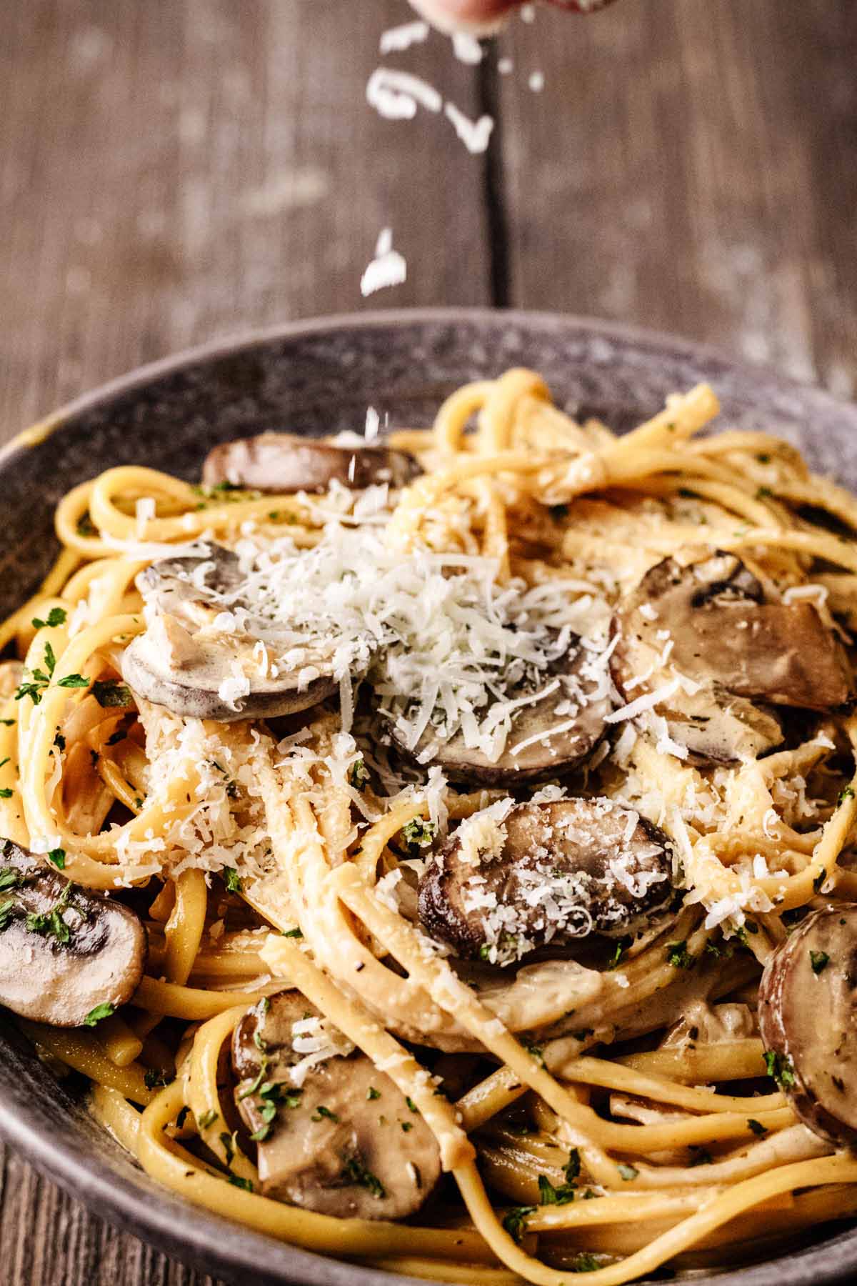 One-pot mushroom pasta in a gray bowl topped with freshly grated Parmesan cheese being sprinkled over the dish.