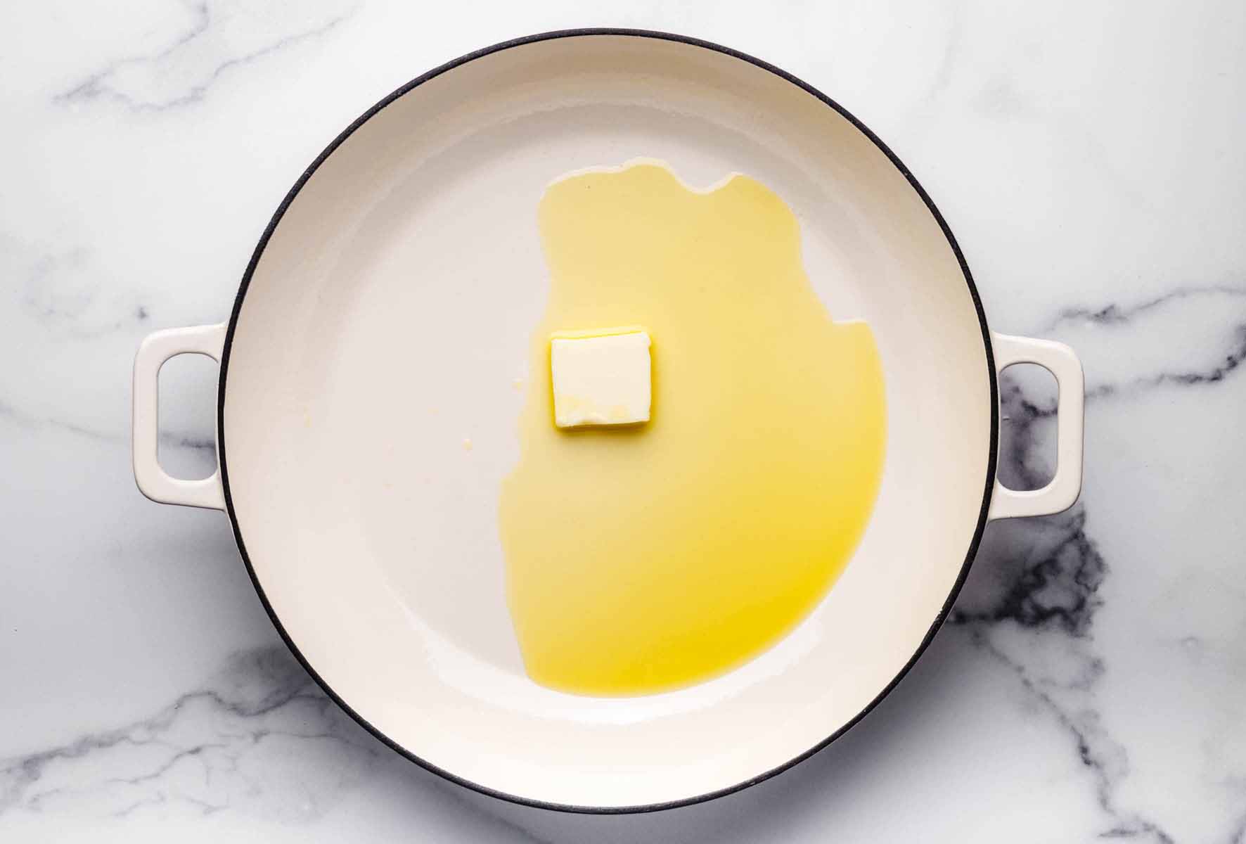 A large white skillet with olive oil and a pat of butter melting, ready to start cooking.