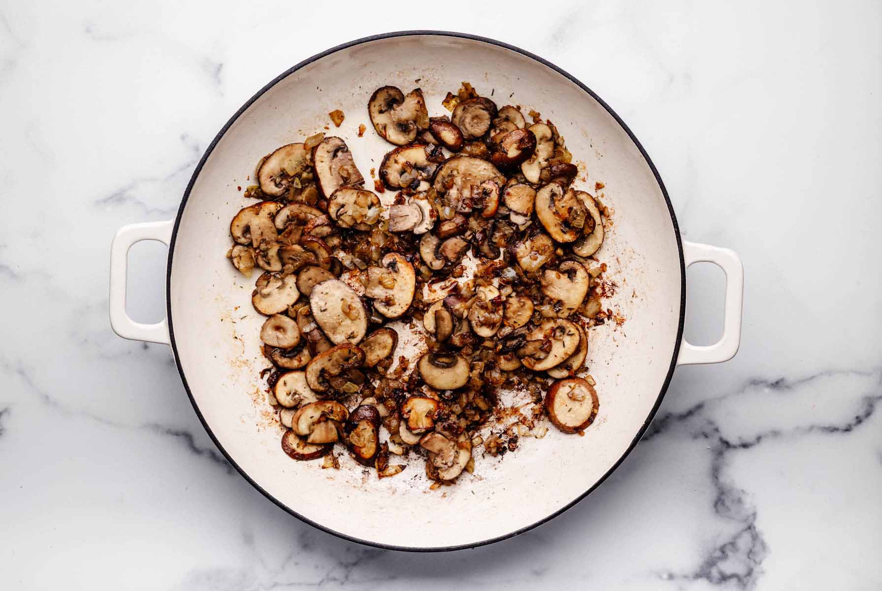 Golden brown sautéed mushrooms, onions, and garlic in a white skillet with a caramelized layer on the bottom of the pan.