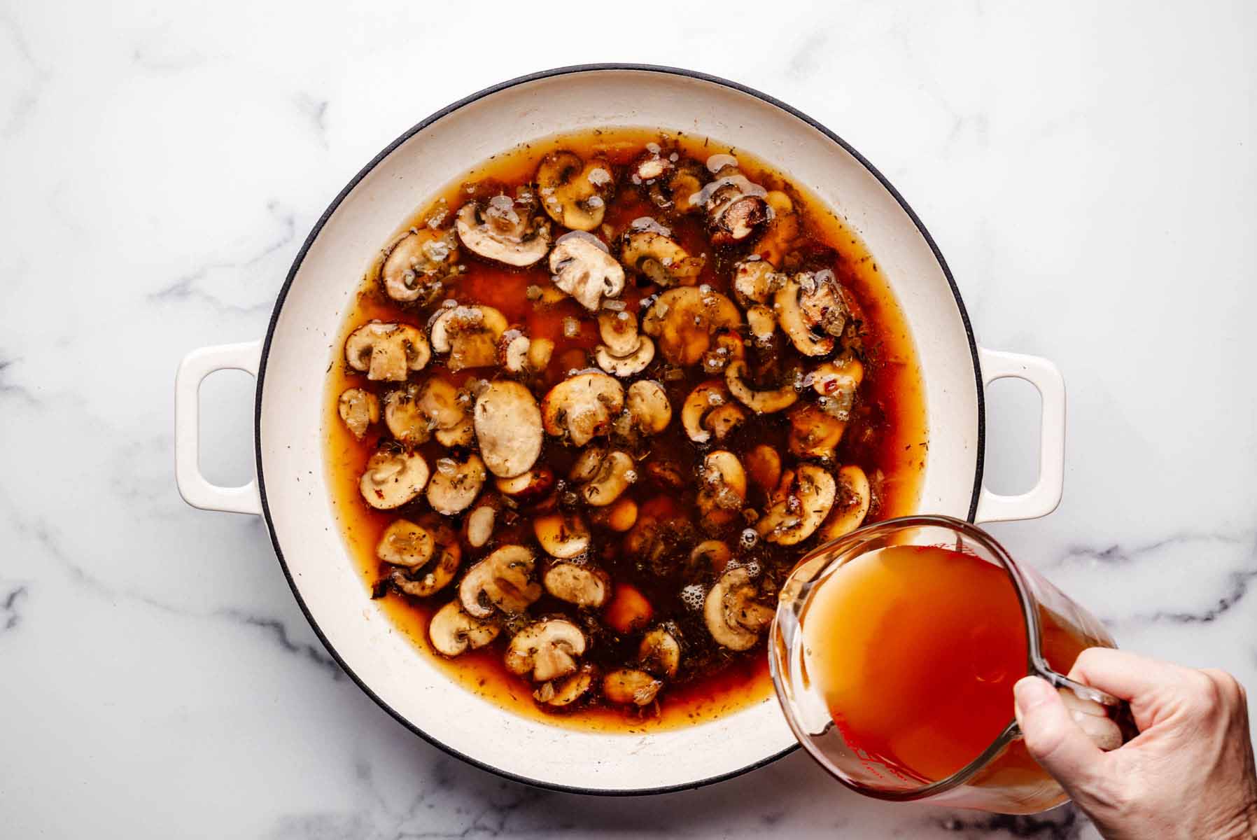 Pouring vegetable broth into a skillet with sautéed mushrooms, onions, and garlic to deglaze the pan.