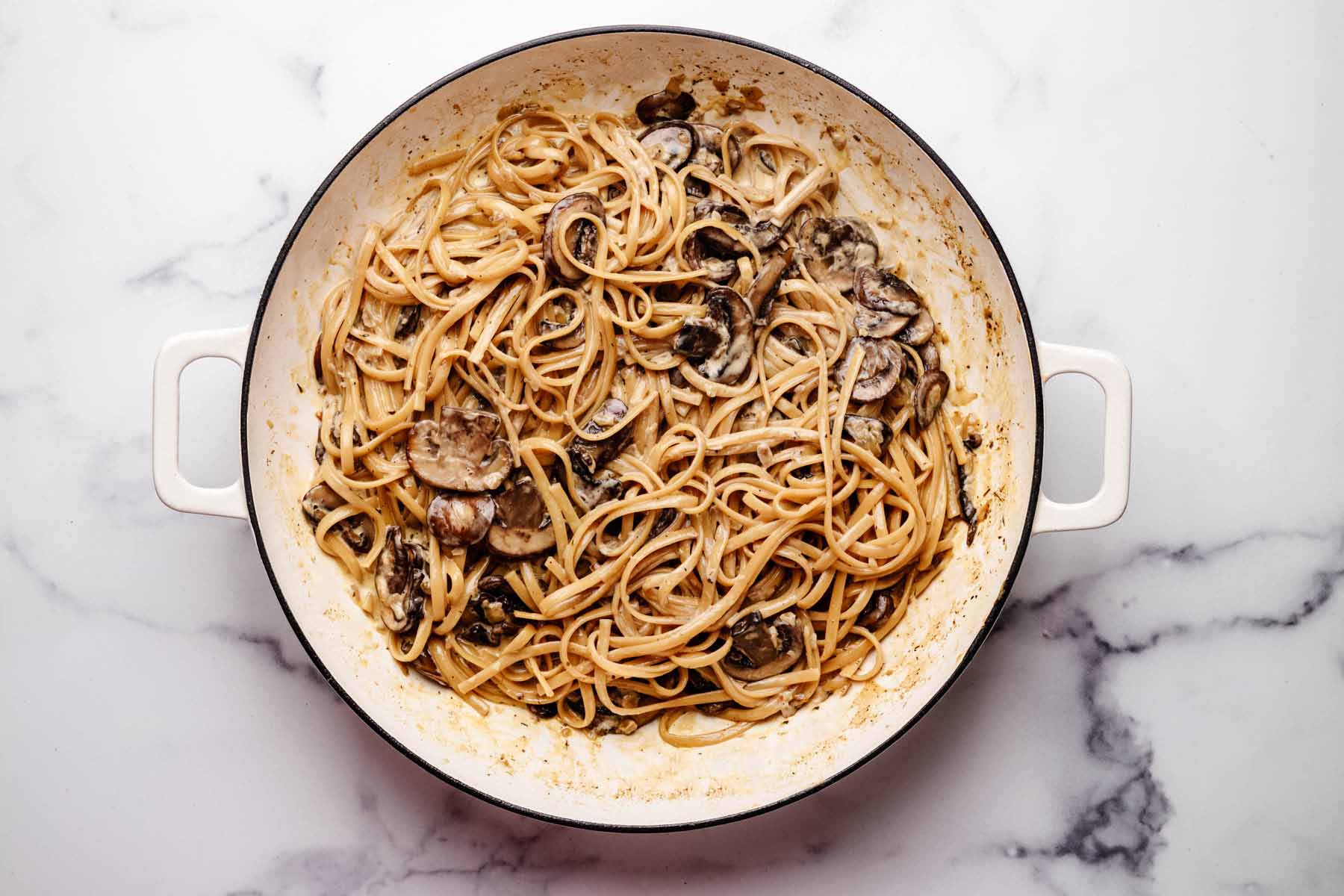 Cooked linguine pasta mixed with sautéed mushrooms and a creamy sauce in a large white pot, ready to be served.