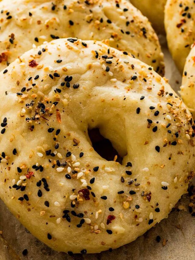Close-up of a freshly baked everything bagel with a golden crust and generous seasoning, resting on parchment paper.