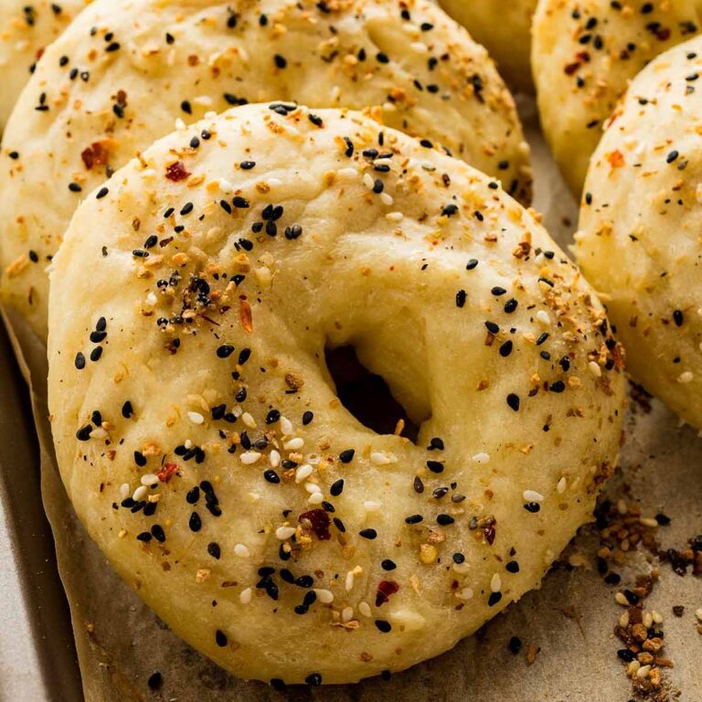 Close-up of a freshly baked everything bagel with a golden crust and generous seasoning, resting on parchment paper.