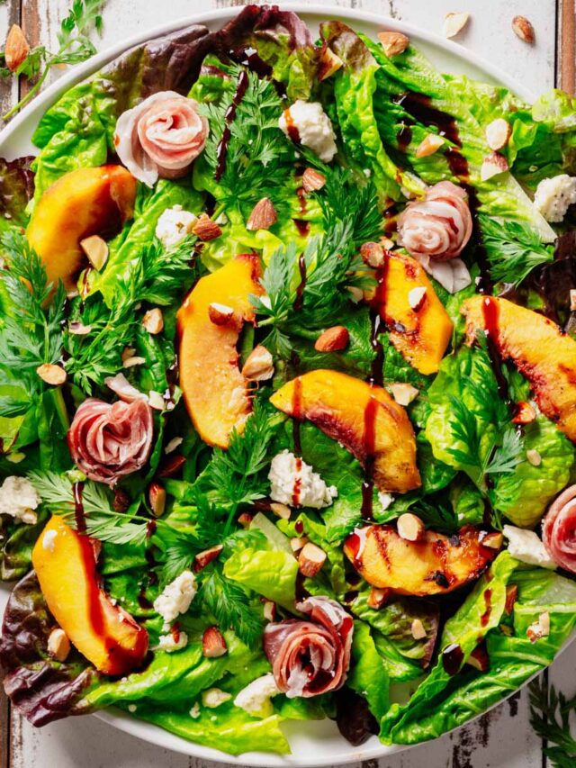 Grilled Peach & Prosciutto Salad with caramelized peaches, prosciutto rosettes, Boursin cheese, toasted almonds, and fresh mixed greens drizzled with balsamic glaze, served on a white plate.