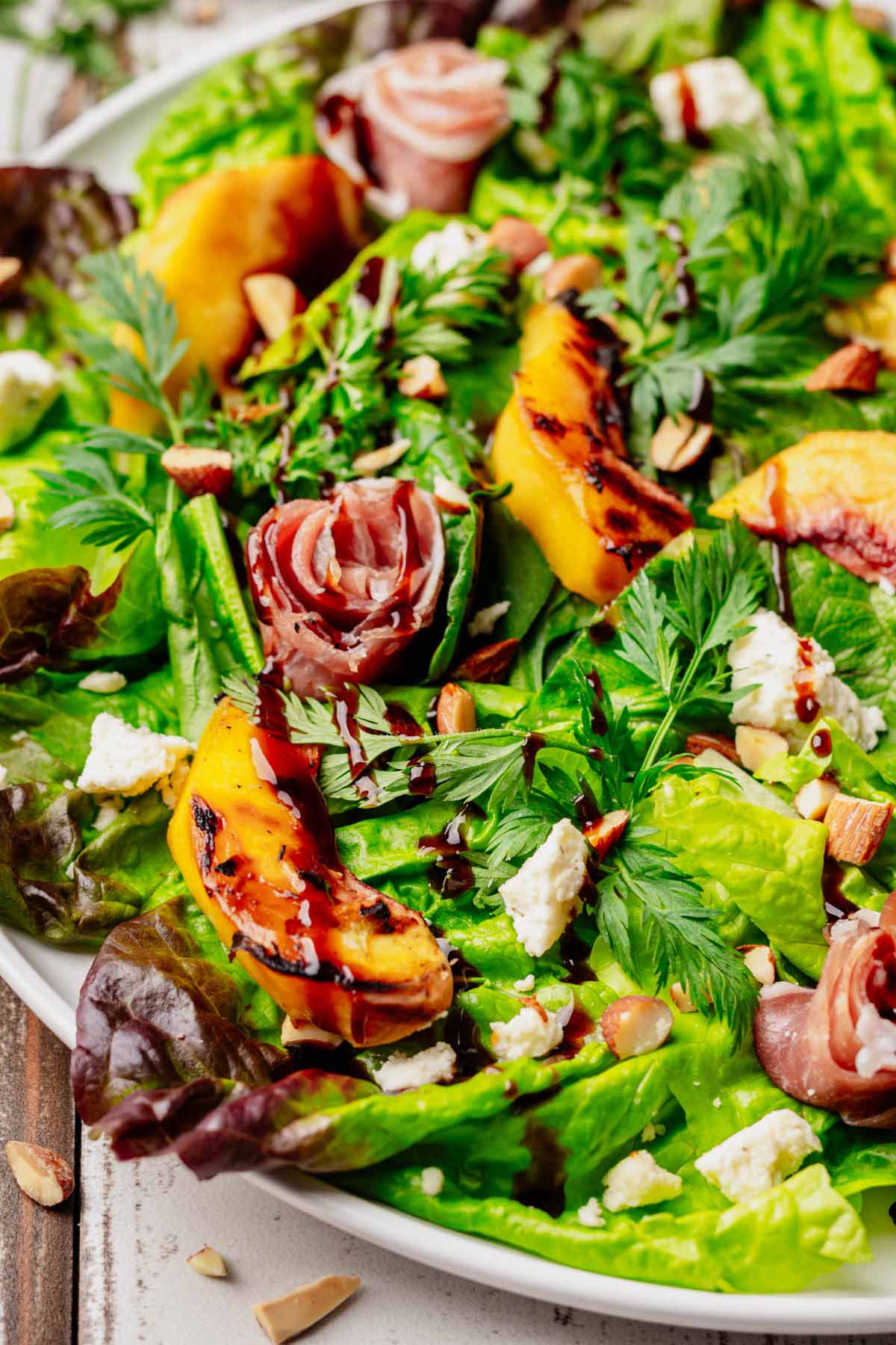 Grilled Peach & Prosciutto Salad close-up featuring caramelized peaches, prosciutto rosettes, Boursin cheese, toasted almonds, and fresh mixed greens drizzled with balsamic glaze.