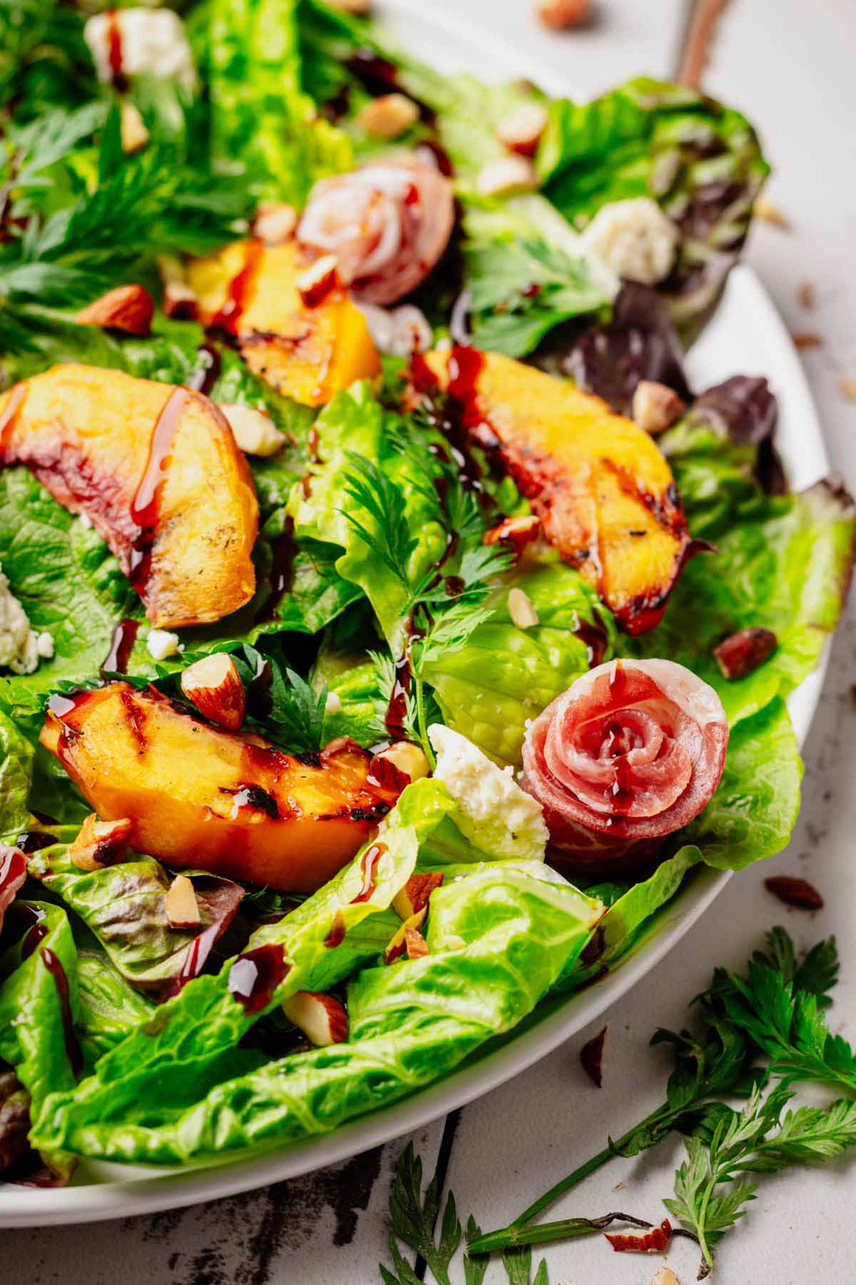 Grilled Peach & Prosciutto Salad close-up with caramelized peaches, prosciutto rosettes, Boursin cheese, toasted almonds, and fresh mixed greens drizzled with balsamic glaze.