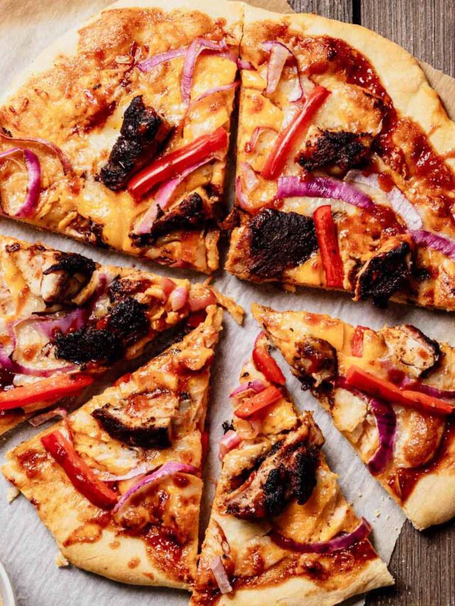 Sliced jerk chicken pizza with BBQ sauce, red onion, red bell pepper, and mango chipotle glaze on parchment paper, with a bowl of extra sauce on the side.
