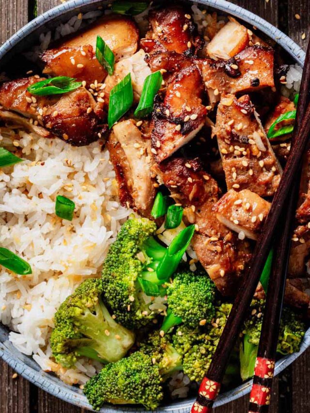 Top-down view of a bowl filled with teriyaki chicken thighs, white rice, and broccoli, garnished with sesame seeds and green onions, with chopsticks resting on the bowl.