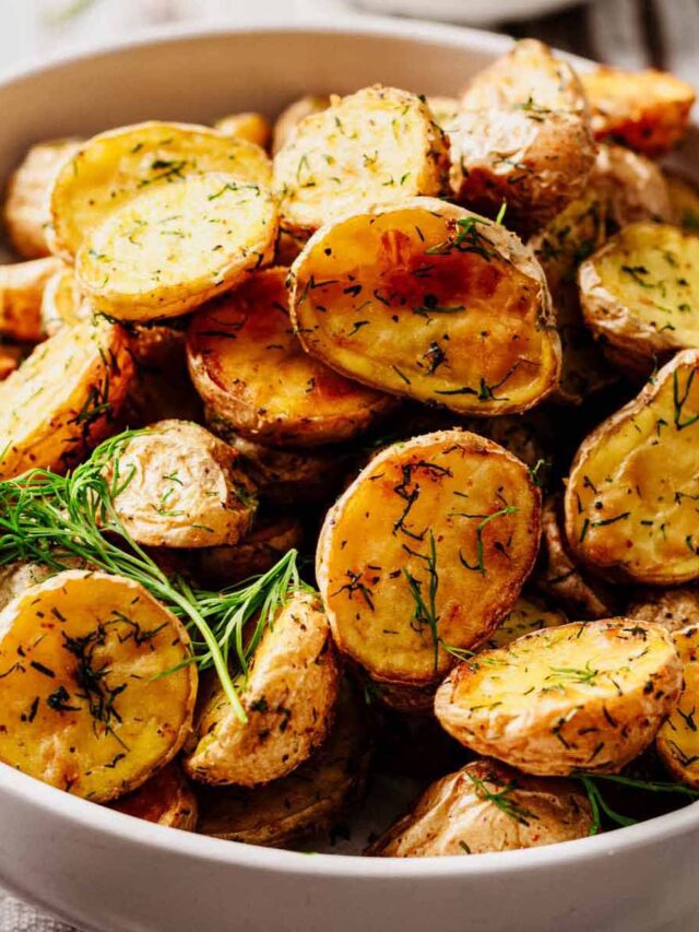 Close-up of golden, crispy dill roasted potatoes in a white bowl, garnished with fresh dill.