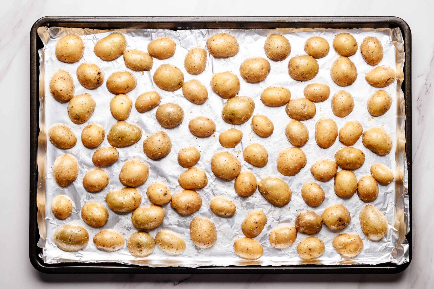 Seasoned baby potatoes arranged cut-side down on a foil-lined baking sheet, ready for roasting.