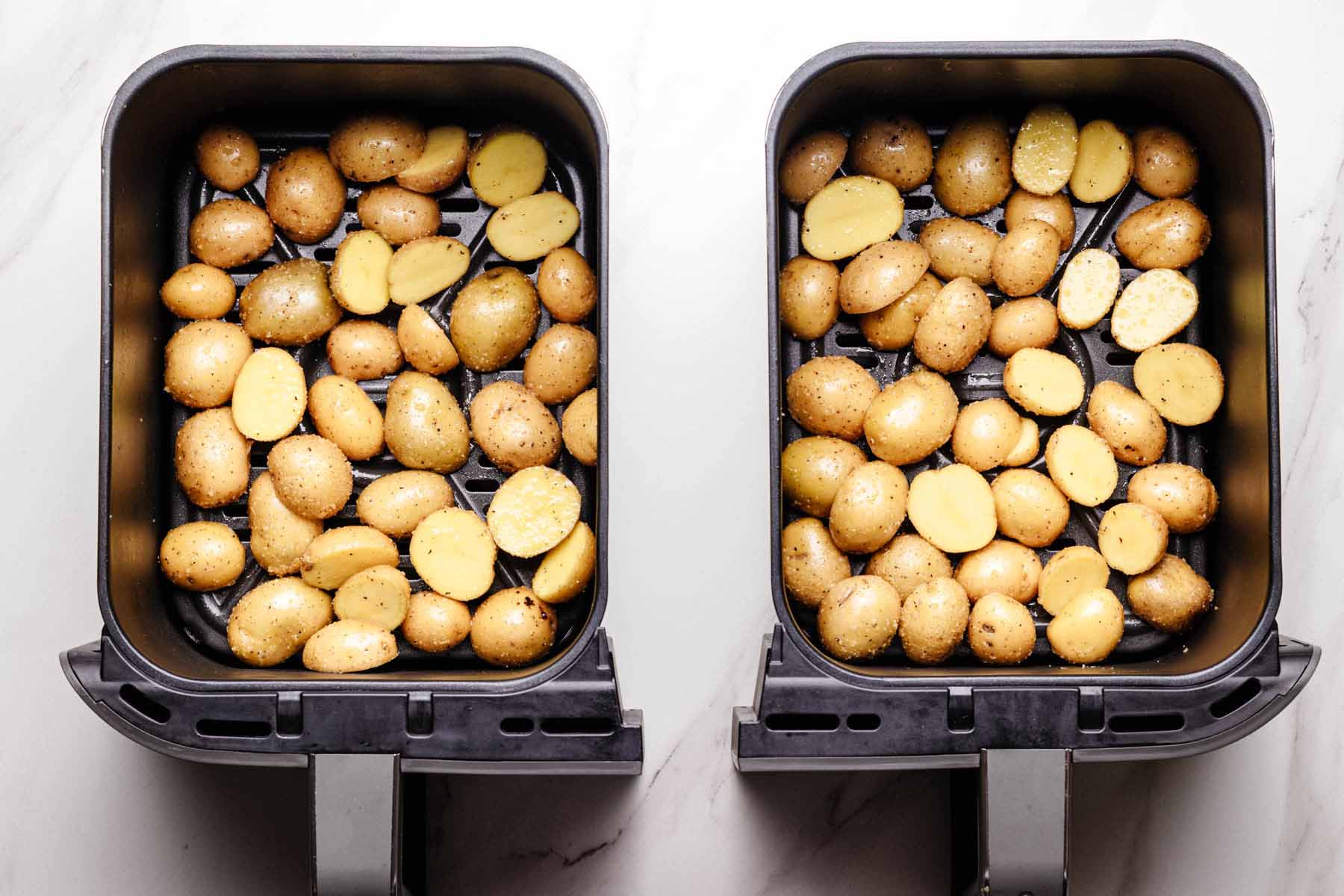 Seasoned baby potatoes arranged in a single layer in two air fryer baskets, ready to cook.