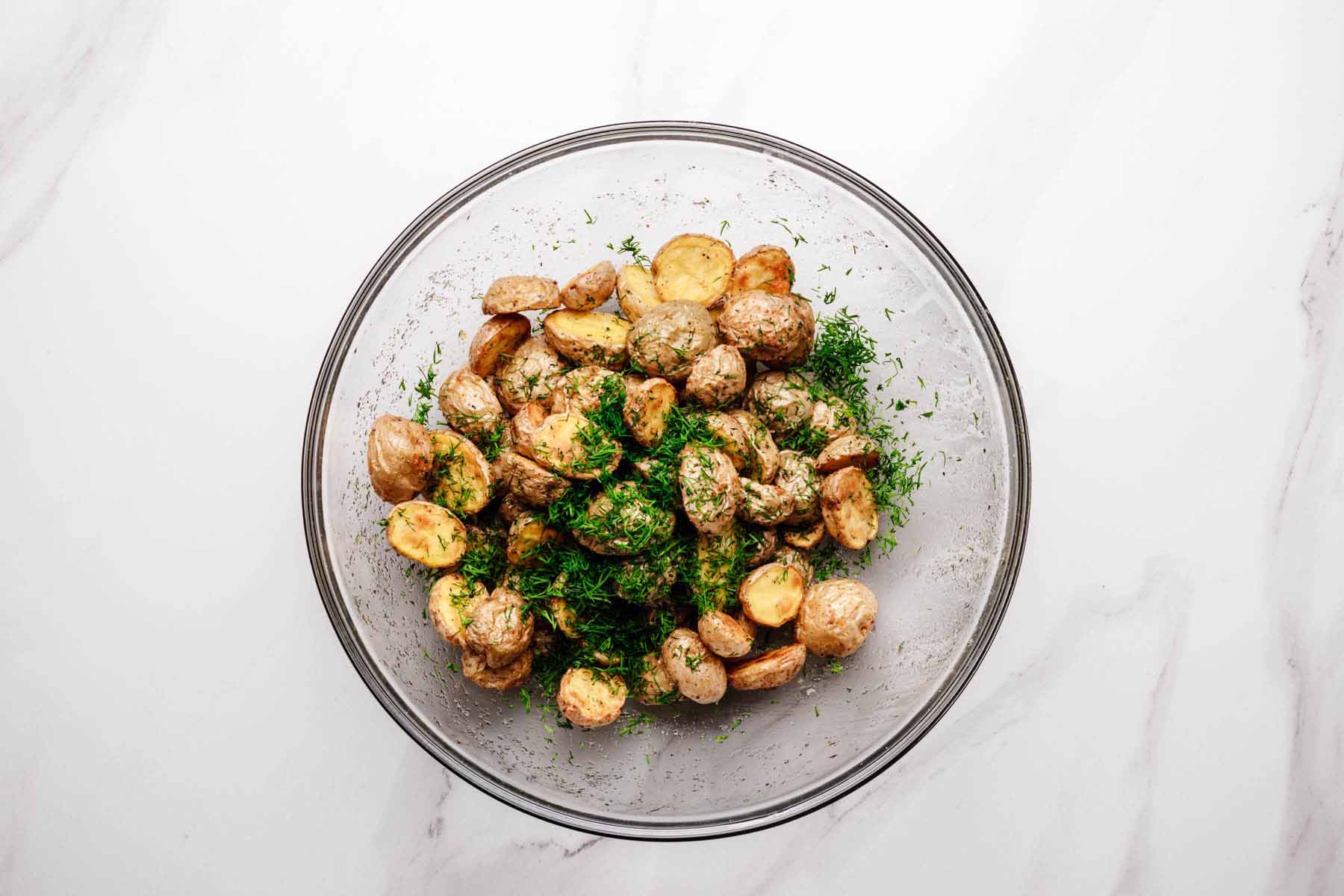 Roasted baby potatoes tossed with chopped fresh dill in a glass mixing bowl.