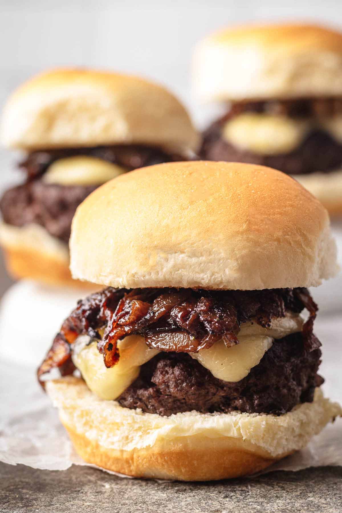 Front-facing view of a French onion slider with melted cheese and caramelized onions, with more sliders blurred in the background.