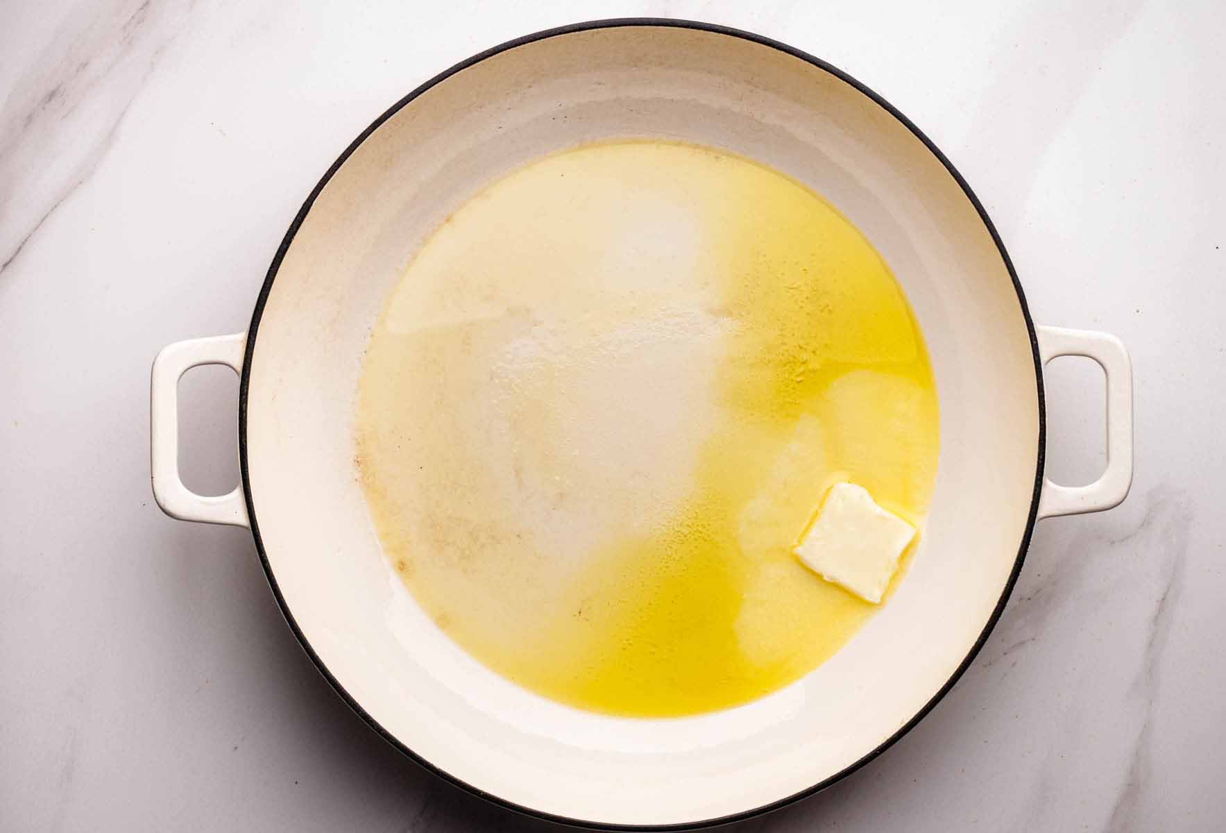 Butter and olive oil melting together in a white skillet, the first step in caramelizing onions.