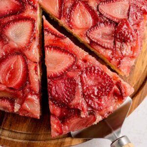 Close-up of strawberry upside down cake with a slice being lifted, showing caramelized baked strawberries on top of a golden, tender cake layer