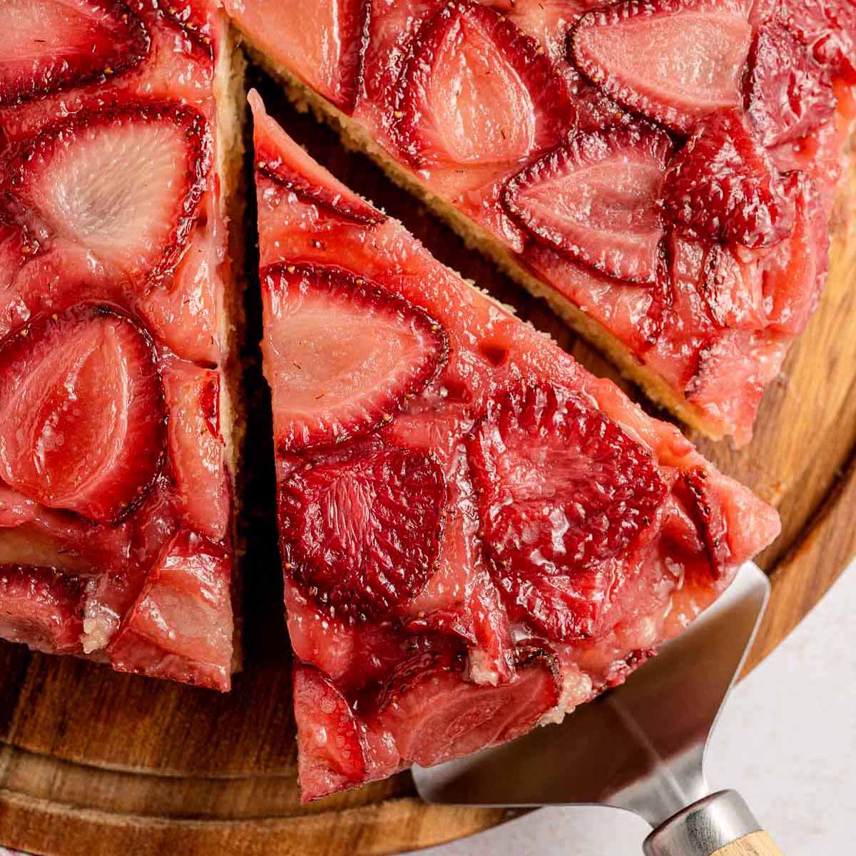 Close-up of strawberry upside down cake with a slice being lifted, showing caramelized baked strawberries on top of a golden, tender cake layer
