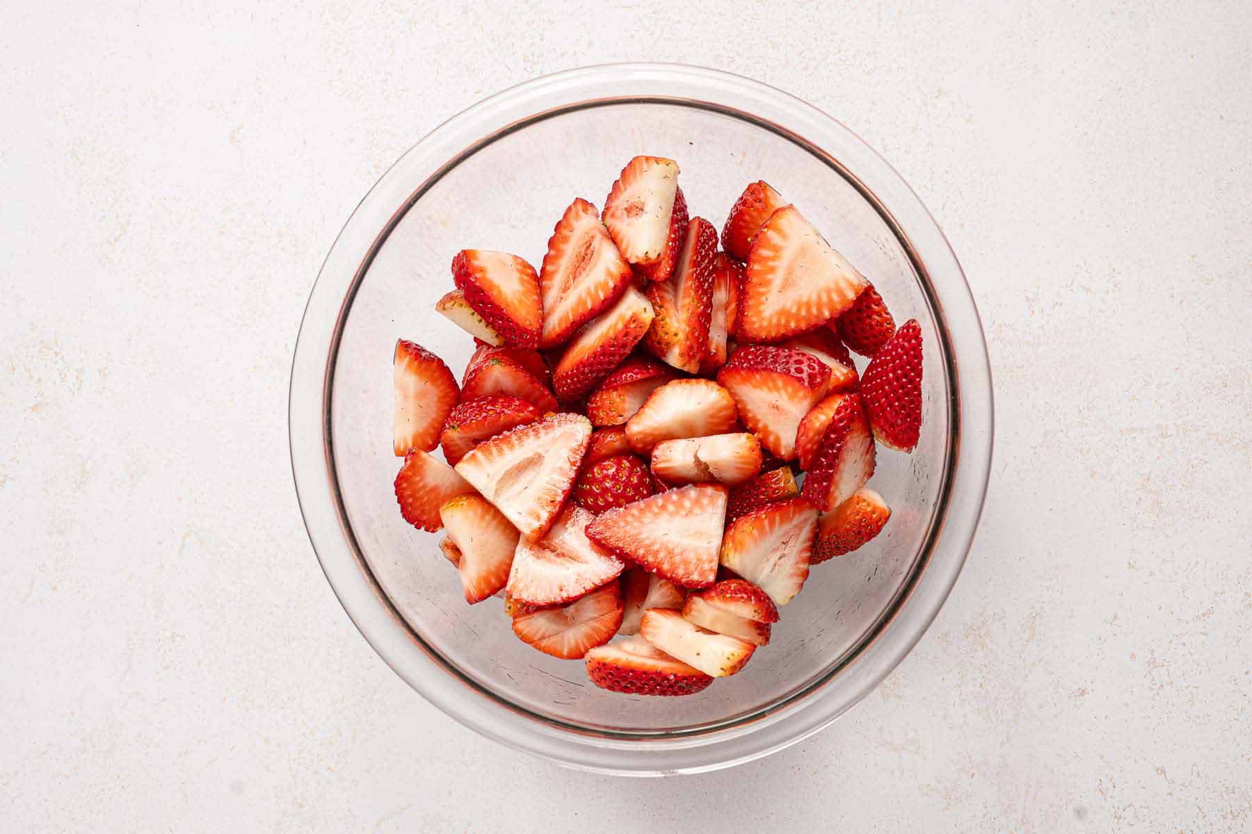 Sliced fresh strawberries in a clear glass bowl on a light surface, ready to be used for strawberry upside down cake