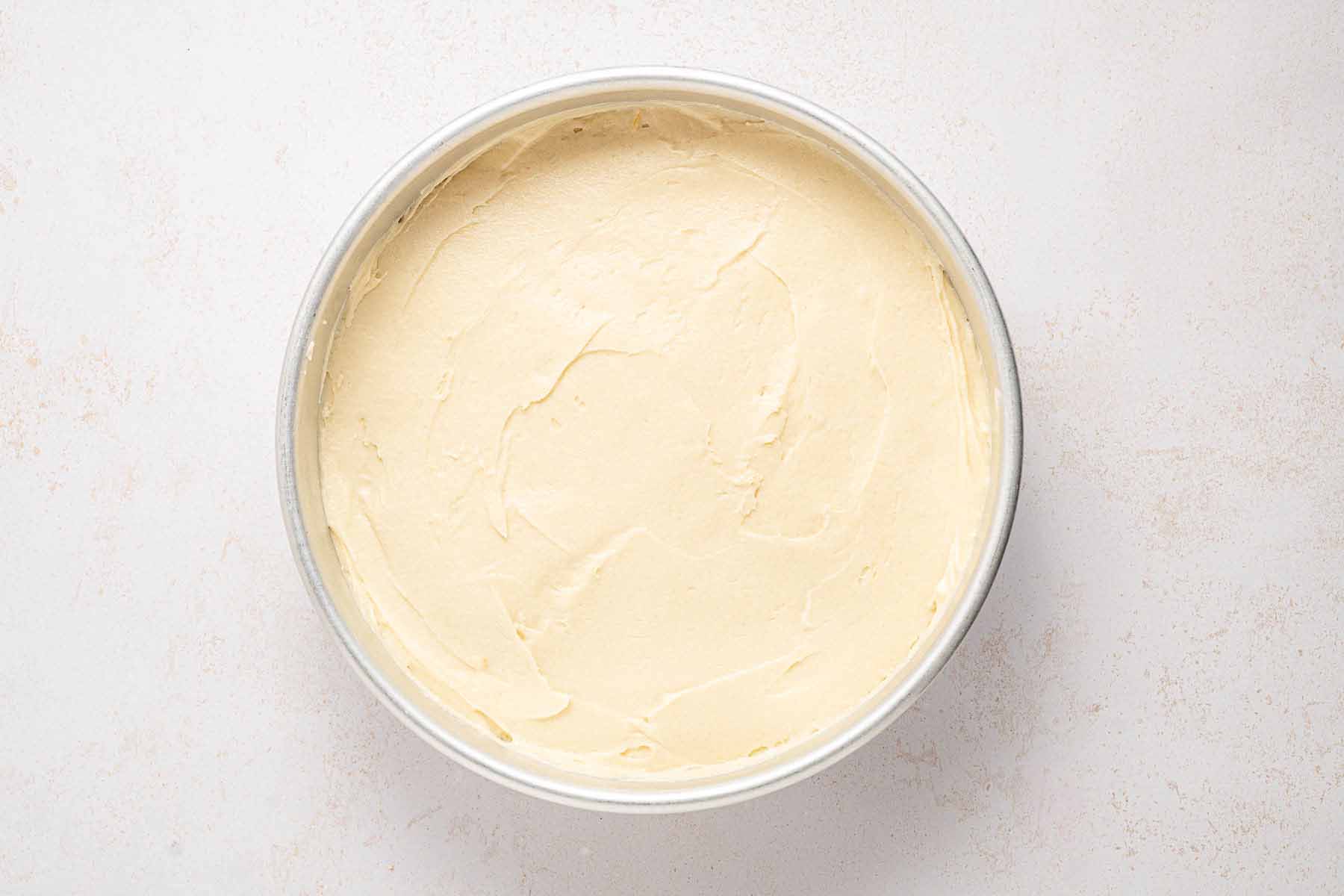 Cake batter spread evenly over the strawberry layer in a round cake pan, ready to bake