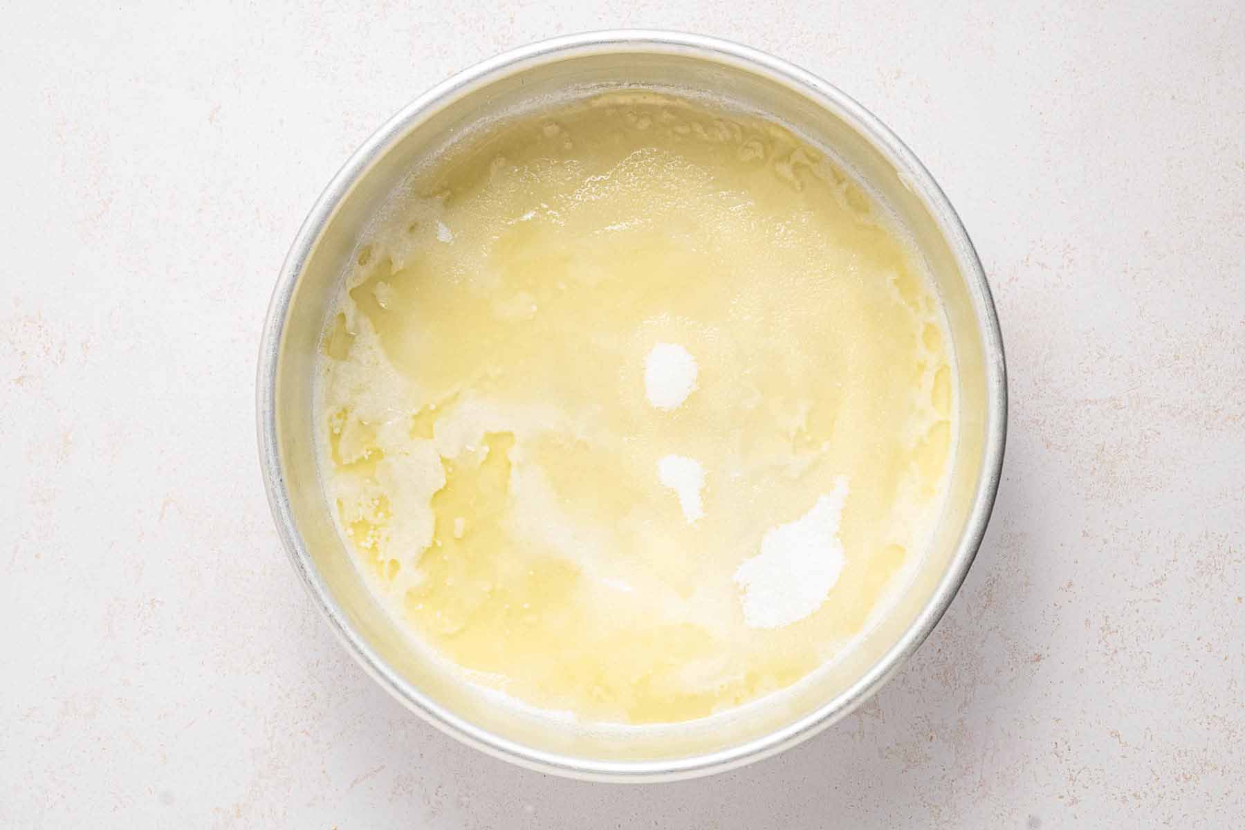 Melted butter spread across the bottom of a round cake pan, the first step in preparing a strawberry upside down cake