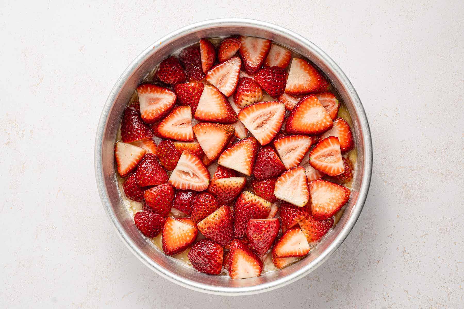 Sliced strawberries arranged in a single layer over melted butter and sugar in a round cake pan, ready to be topped with cake batter