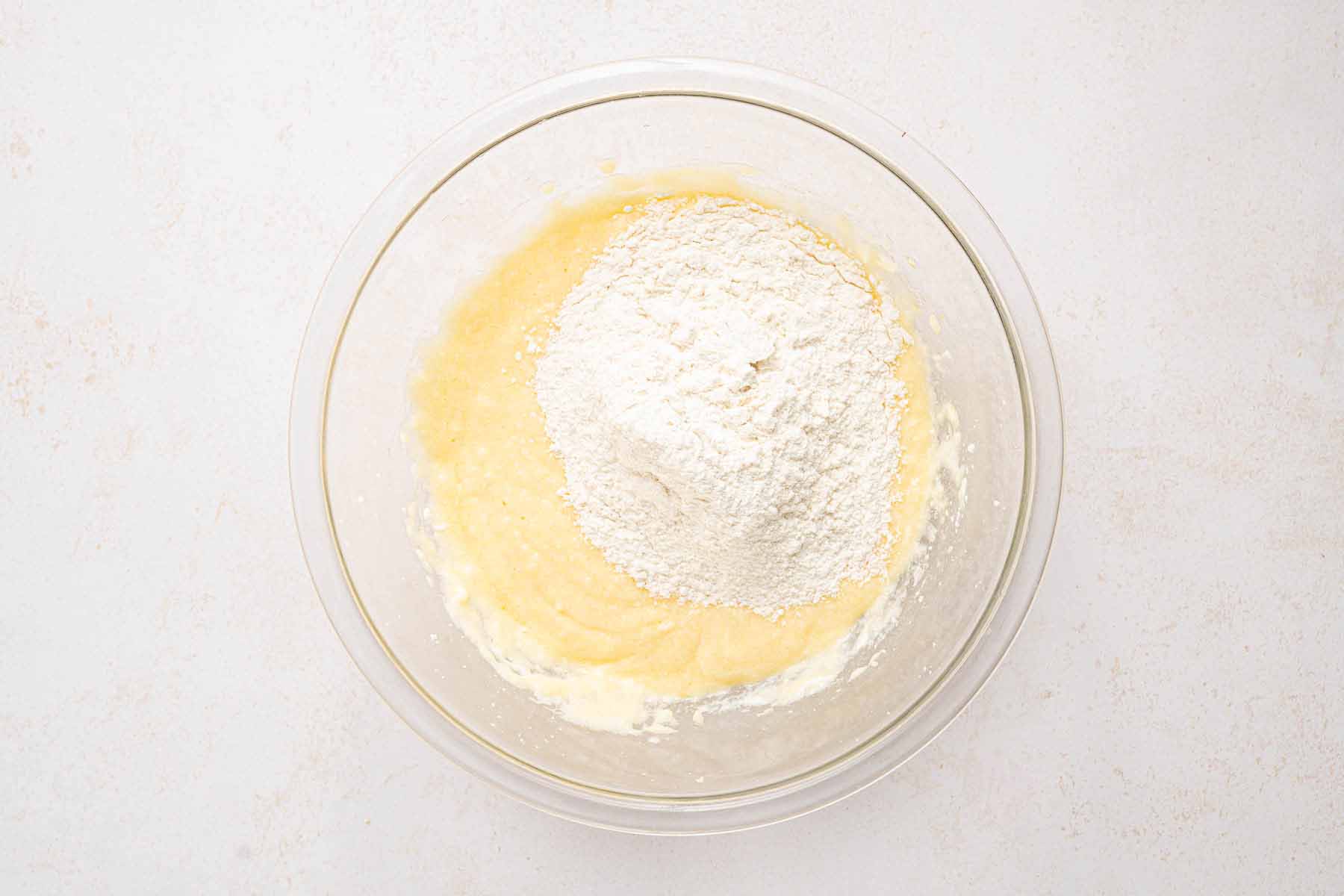 Dry ingredients added to the wet cake batter in a glass bowl, ready to be mixed for strawberry upside down cake