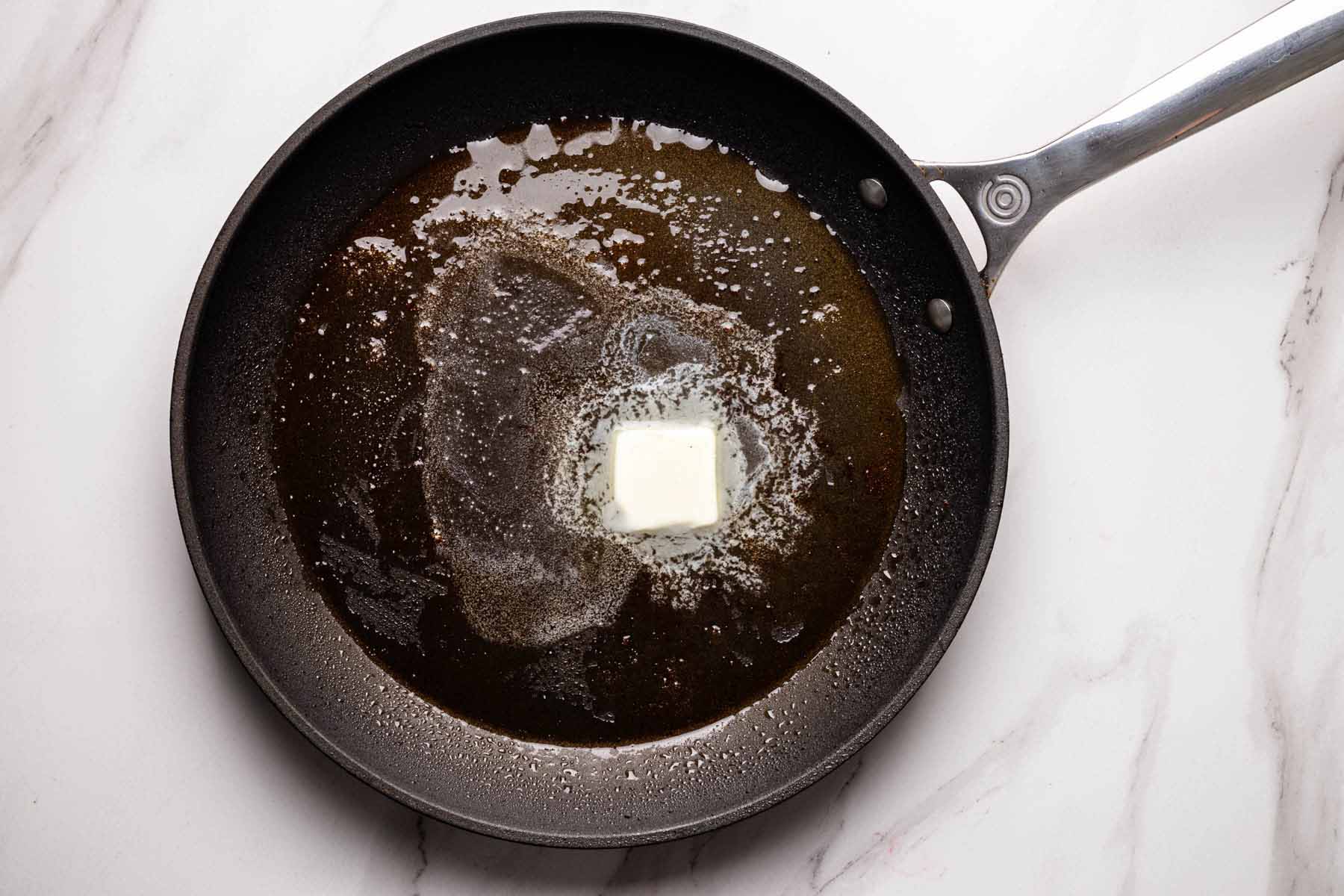 Overhead view of a skillet with melted butter sizzling in shrimp drippings, preparing to sauté garlic and sun-dried tomatoes.