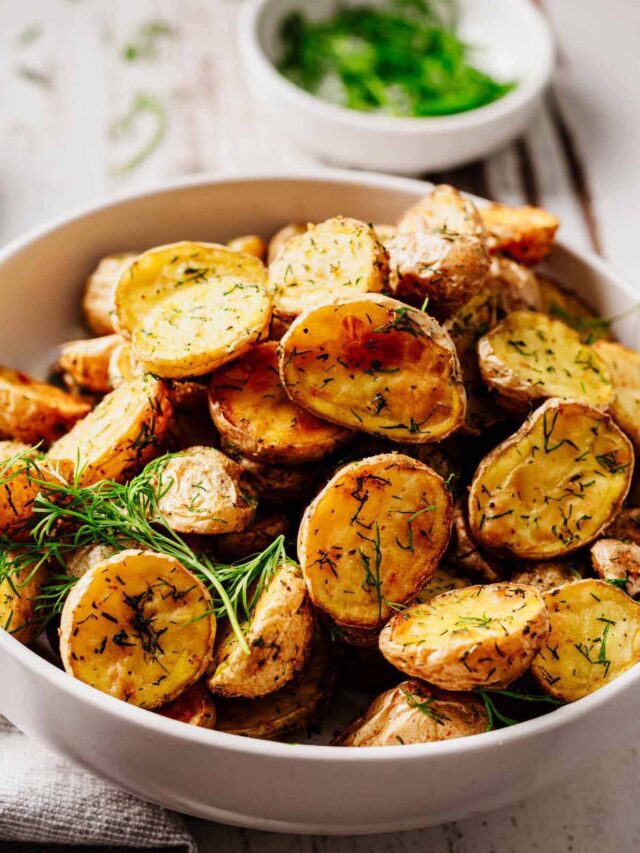 Crispy roasted baby potatoes with fresh dill in a white bowl, styled with herbs and a rustic background