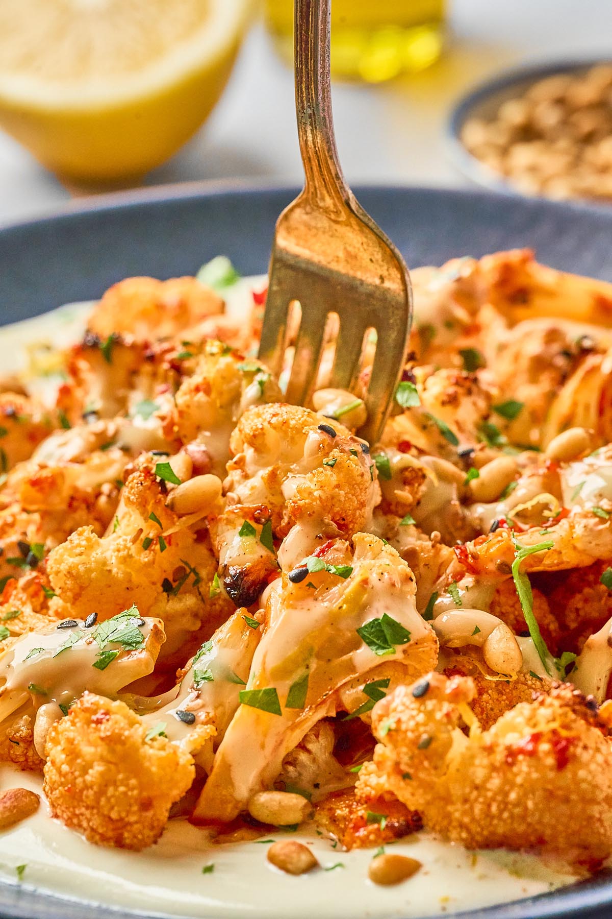 Close-up of a fork lifting harissa roasted cauliflower with whipped cottage cheese, honey-tahini drizzle, toasted pine nuts, and fresh herbs.