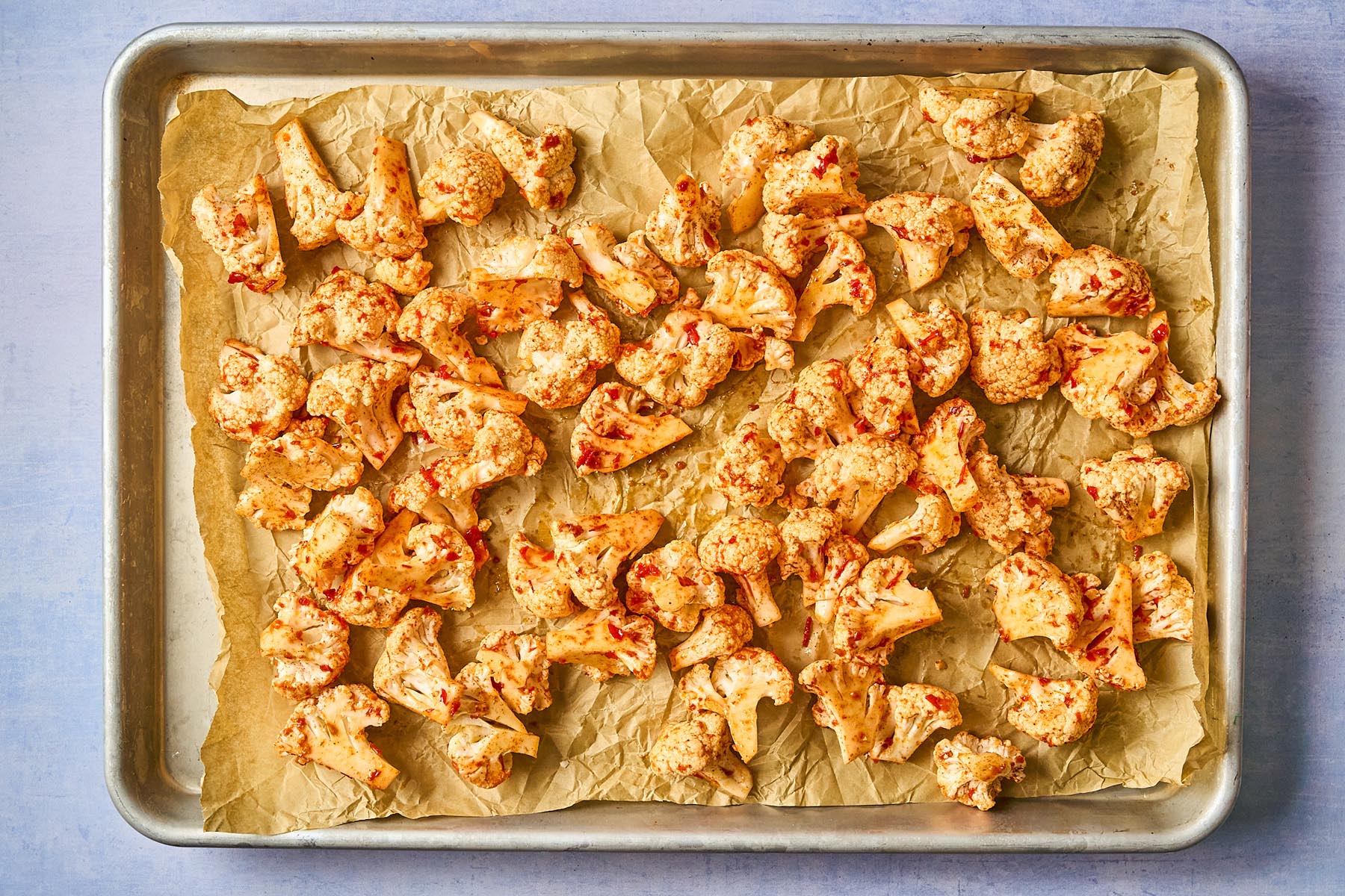 Harissa-coated cauliflower florets arranged in a single layer on a parchment-lined baking sheet, ready to be roasted.