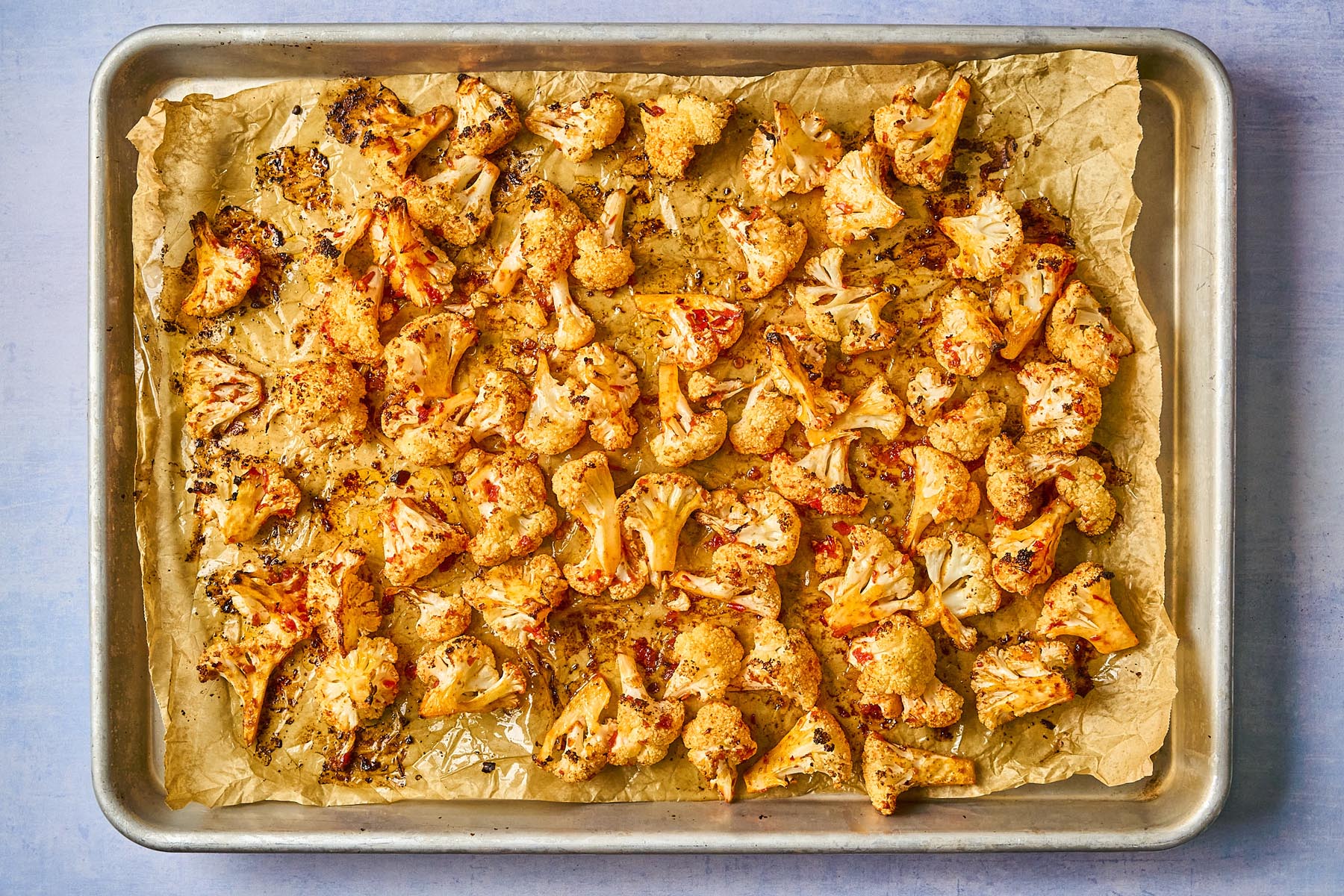 Harissa roasted cauliflower on a parchment-lined baking sheet, golden brown with caramelized edges after roasting.