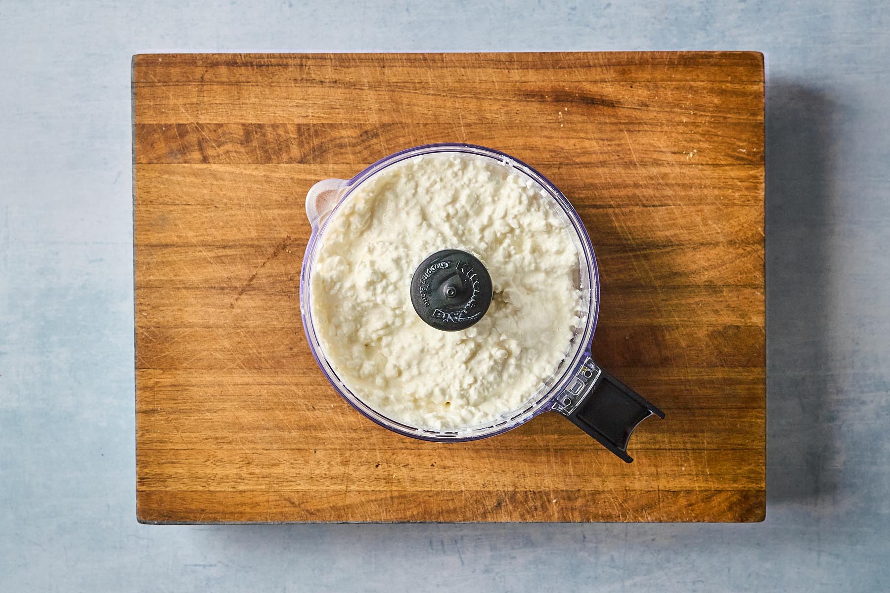 Cottage cheese in a food processor bowl, ready to be blended into a smooth whipped spread.