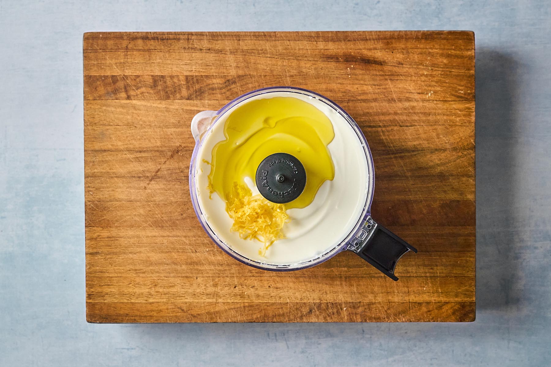 Whipped cottage cheese mixture in a food processor, topped with olive oil and fresh lemon zest before blending.