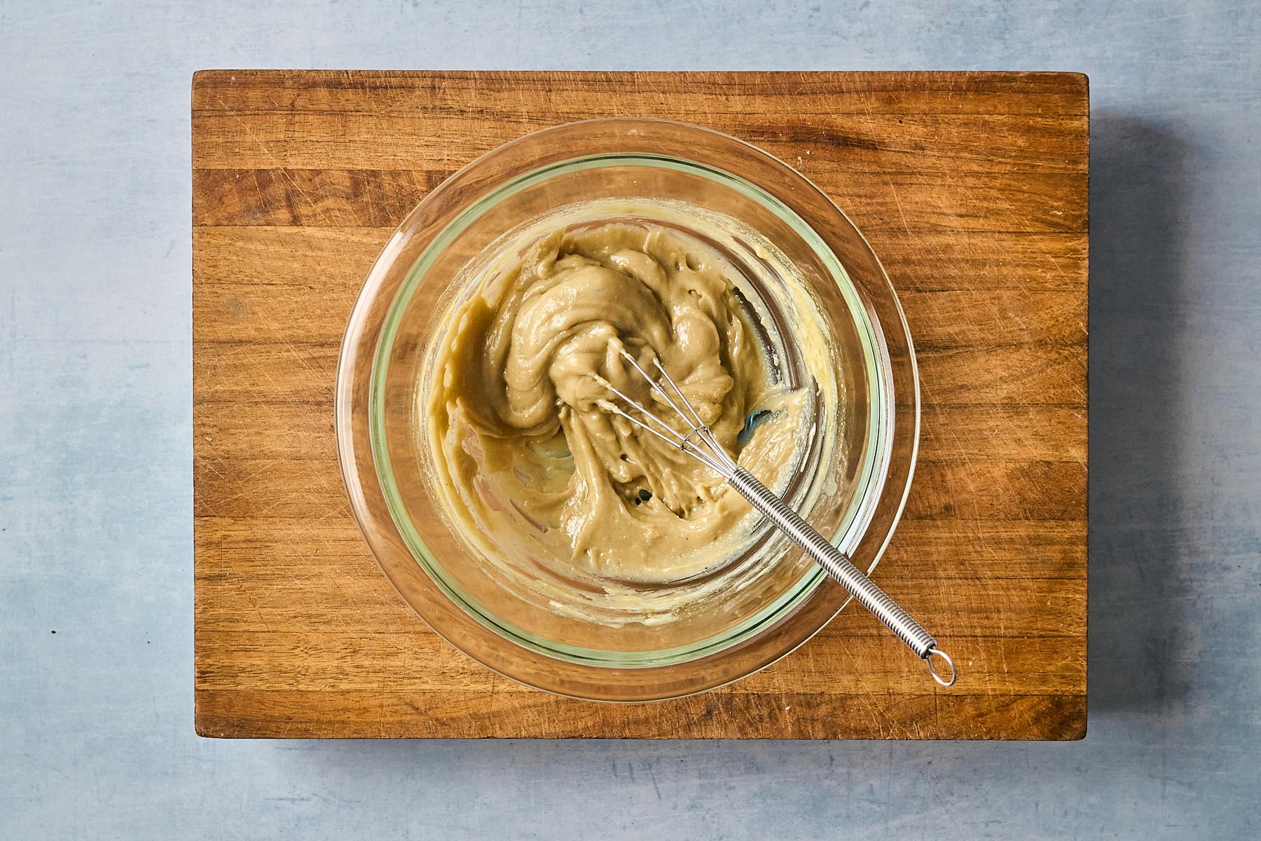 Thick tahini mixture in a glass bowl with a small whisk, partially combined before thinning with water.