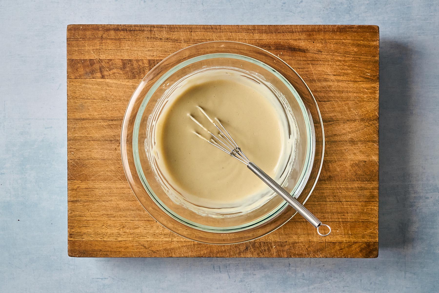 Smooth honey-tahini sauce in a glass bowl with a whisk, blended to a creamy, pourable consistency.