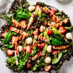 Strawberry chicken Caprese salad served on a white plate, featuring mixed greens, grilled chicken strips, fresh strawberries, mozzarella balls, chopped pecans, basil leaves, and a drizzle of balsamic glaze.