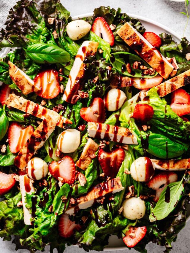 Strawberry chicken Caprese salad served on a white plate, featuring mixed greens, grilled chicken strips, fresh strawberries, mozzarella balls, chopped pecans, basil leaves, and a drizzle of balsamic glaze.