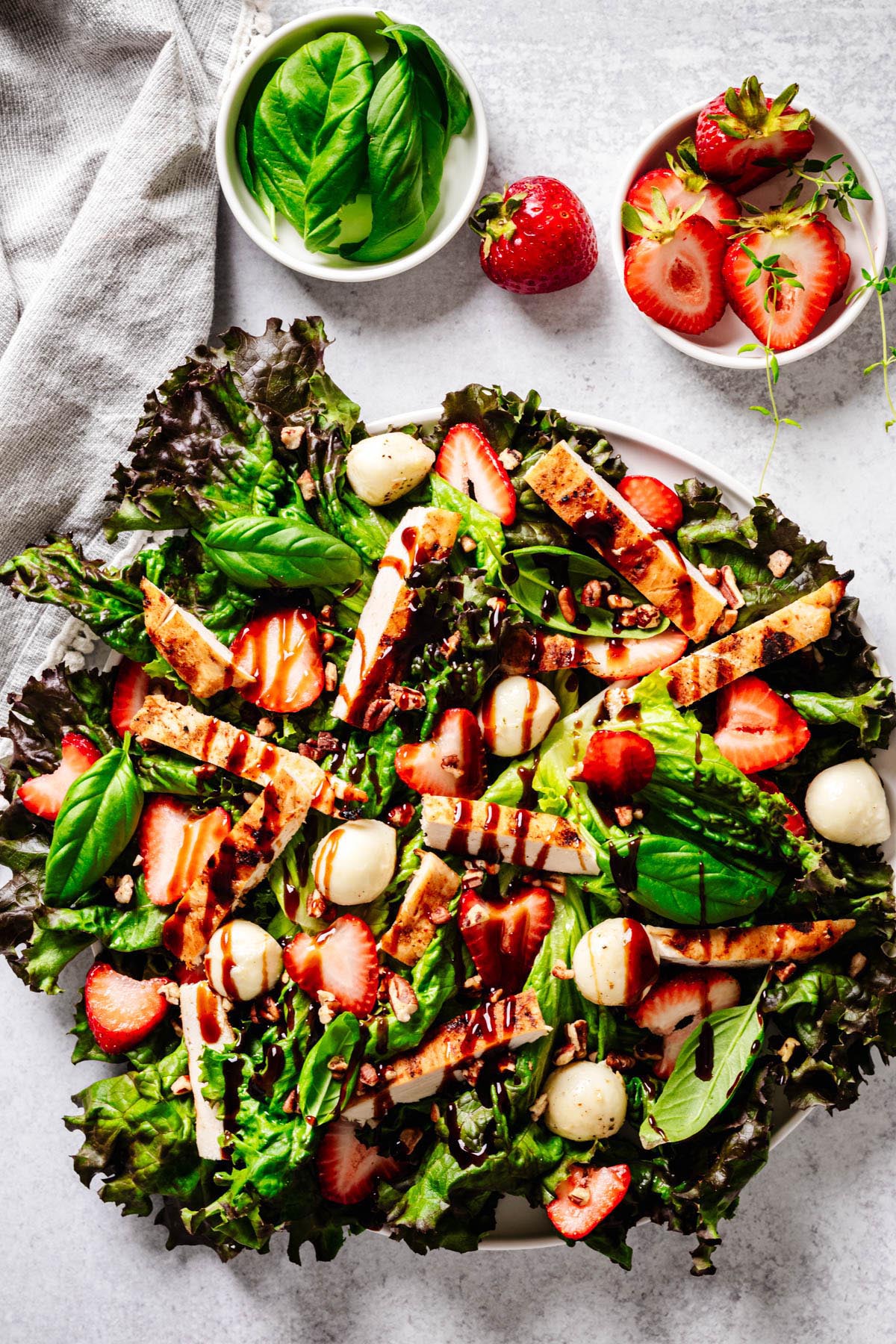 The highest screening of the strawberry chicken salad, strawberries, mozzars, mozzarella balls, leaves, pecams are mixed, served in a white plate with small Basil dishes and nearby strawberry.