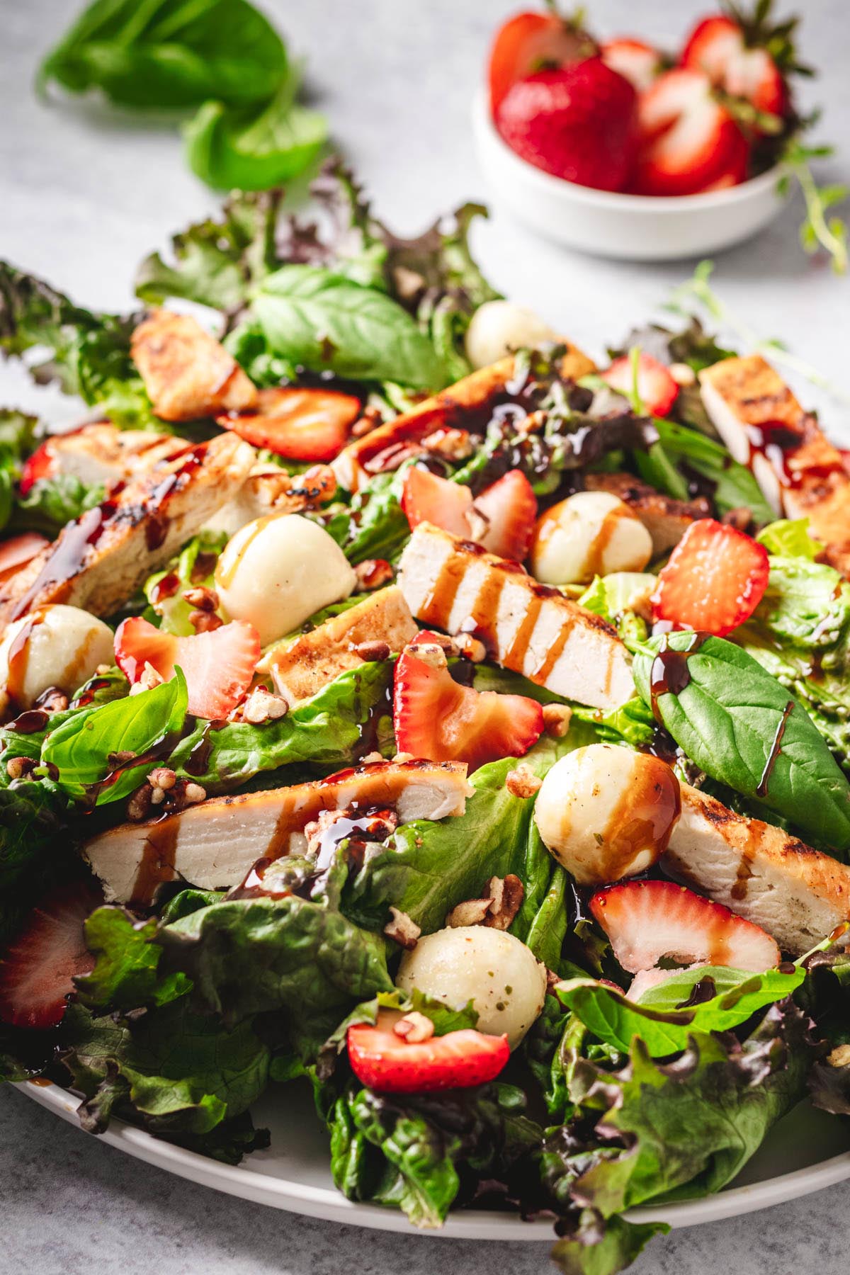 Angle-up angle of a strawberry chicken salad, indicating the grazing chicken strips, strips of foods of mozzarella, basil leaves.