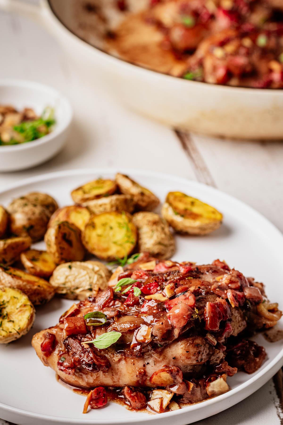 Plated strawberry chicken topped with strawberry balsamic glaze and toasted almonds, served with roasted baby potatoes on a white plate.