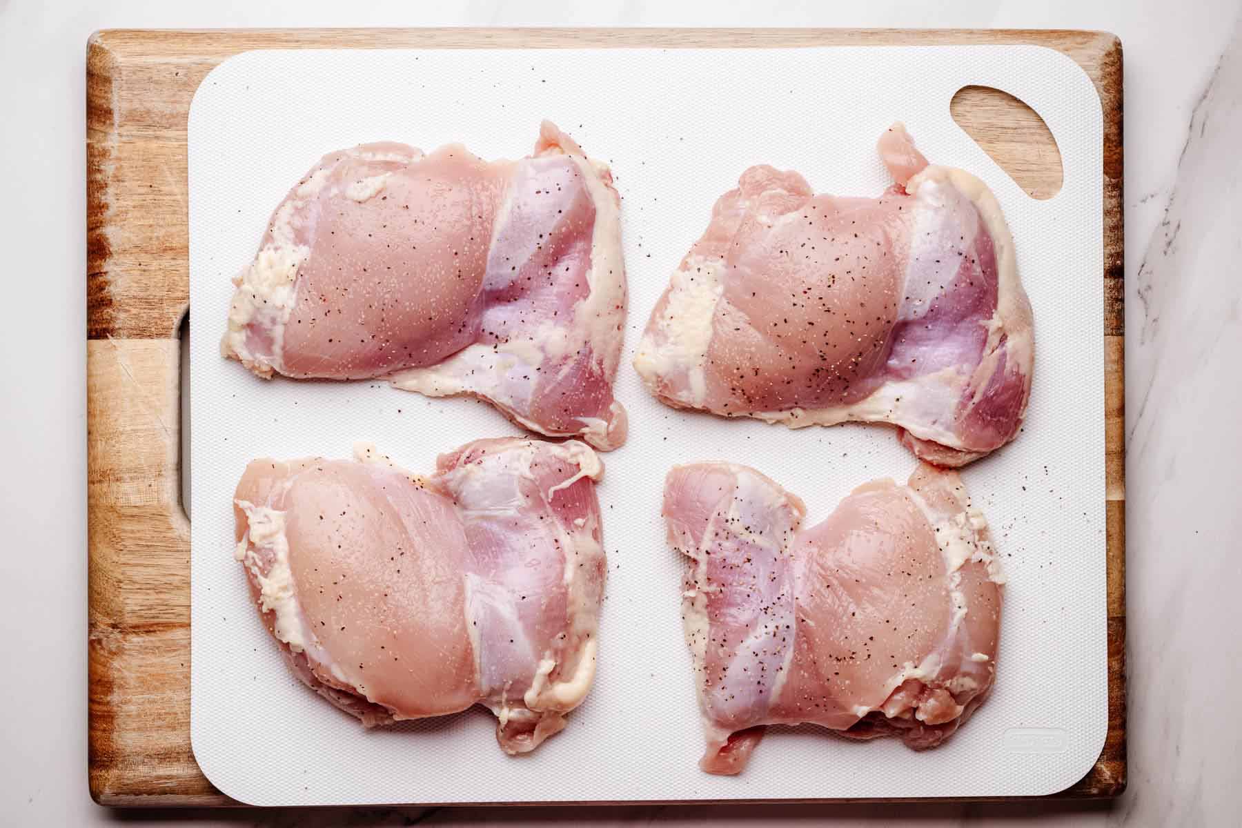 Raw, seasoned chicken thighs arranged on a white cutting board set over a wooden board.